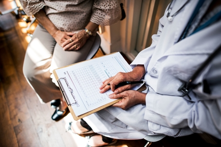 Doctor holding a clipboard and pen while speaking with a patient.