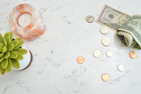 Flat lay with money, salt lamp, and potted succulent on a marble surface.