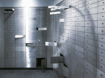 A vault room features walls of grey metal safe deposit boxes, some ajar with keys visible, suggesting security.