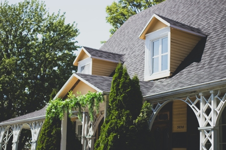 A picturesque yellow house boasts intricate white trim and dormer windows under a dark grey roof.