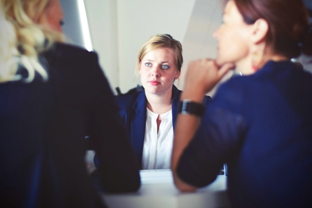 A young woman sits across from two people, likely in a job interview, as she looks intently forward.