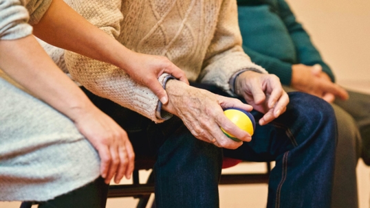 A person is holding the arm of an elderly adult holding a stress ball.